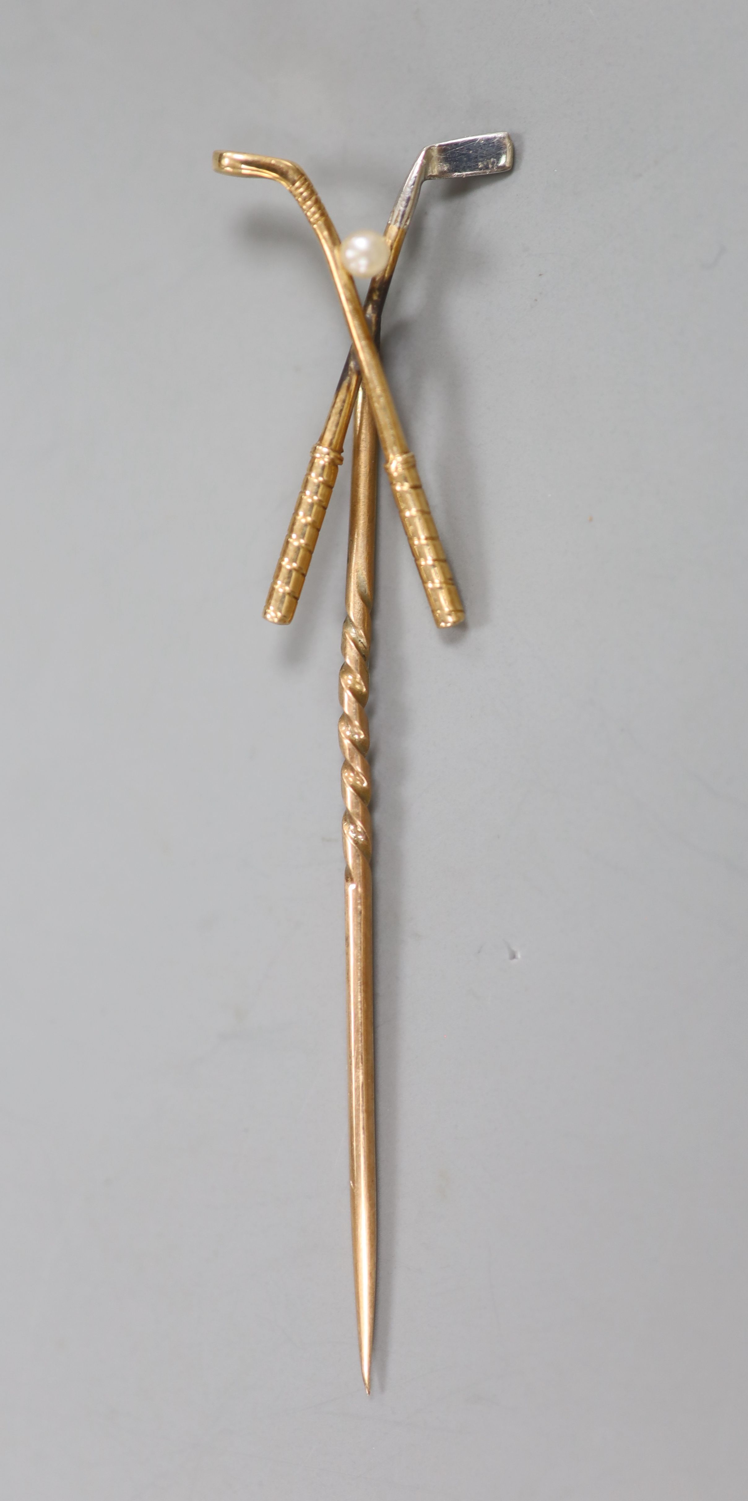 An early 20th century yellow metal and seed pearl set crossed golf clubs stick pin, 57mm, gross 1.6 grams.